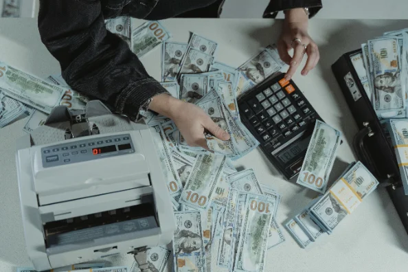 Manos contando billetes junto a una máquina contadora y una calculadora