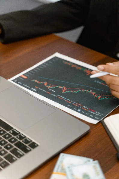 Persona señalando un gráfico financiero impreso junto a una notebook