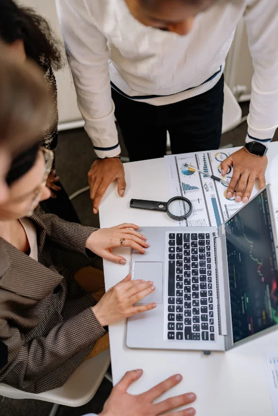 Equipo revisando planillas y gráficos impresos con una lupa junto a una notebook